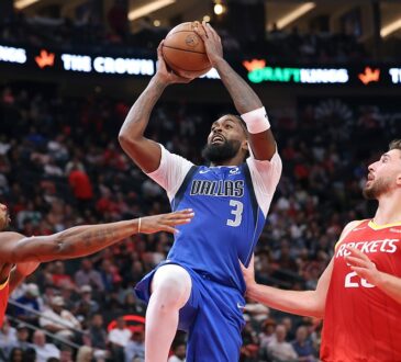 Dallas Mavericks forward Naji Marshall rises with the ball overhead between two Houston Rockets defenders.