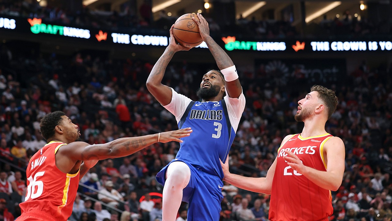 Dallas Mavericks forward Naji Marshall rises with the ball overhead between two Houston Rockets defenders.