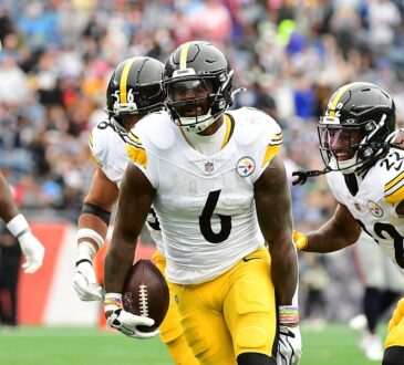 Steelers linebacker Patrick Queen carries the ball after an interception as teammates rush to celebrate.