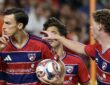 FC Dallas forward Petar Musa holds a finger to his lips while carrying the ball as teammates join him.