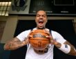 Dallas Mavericks forward P.J. Washington yells while gripping a basketball beneath a Mavericks logo and scoreboard.