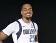 Dallas Mavericks forward P.J. Washington smiles with his hands on his hips in a white Dallas jersey against a black backdrop.