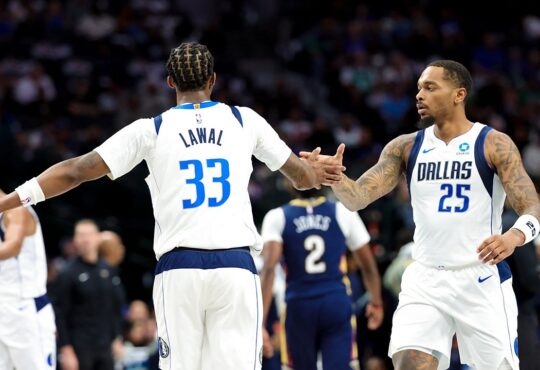 Dallas Mavericks forward P.J. Washington slaps hands with forward Tobi Lawal, who has his back to the camera.