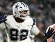 Dallas Cowboys defensive tackle Quinnen Williams raises both gloved hands in celebration as Eagles linemen stand nearby.