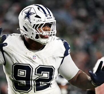 Dallas Cowboys defensive tackle Quinnen Williams raises both gloved hands in celebration as Eagles linemen stand nearby.