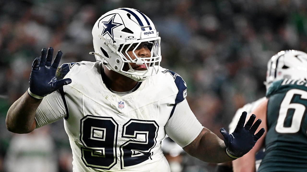 Dallas Cowboys defensive tackle Quinnen Williams raises both gloved hands in celebration as Eagles linemen stand nearby.