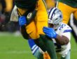Dallas Cowboys defensive tackle Quinnen Williams grabs the legs of the Green Bay Packers quarterback with both gloved hands.