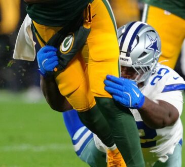 Dallas Cowboys defensive tackle Quinnen Williams grabs the legs of the Green Bay Packers quarterback with both gloved hands.