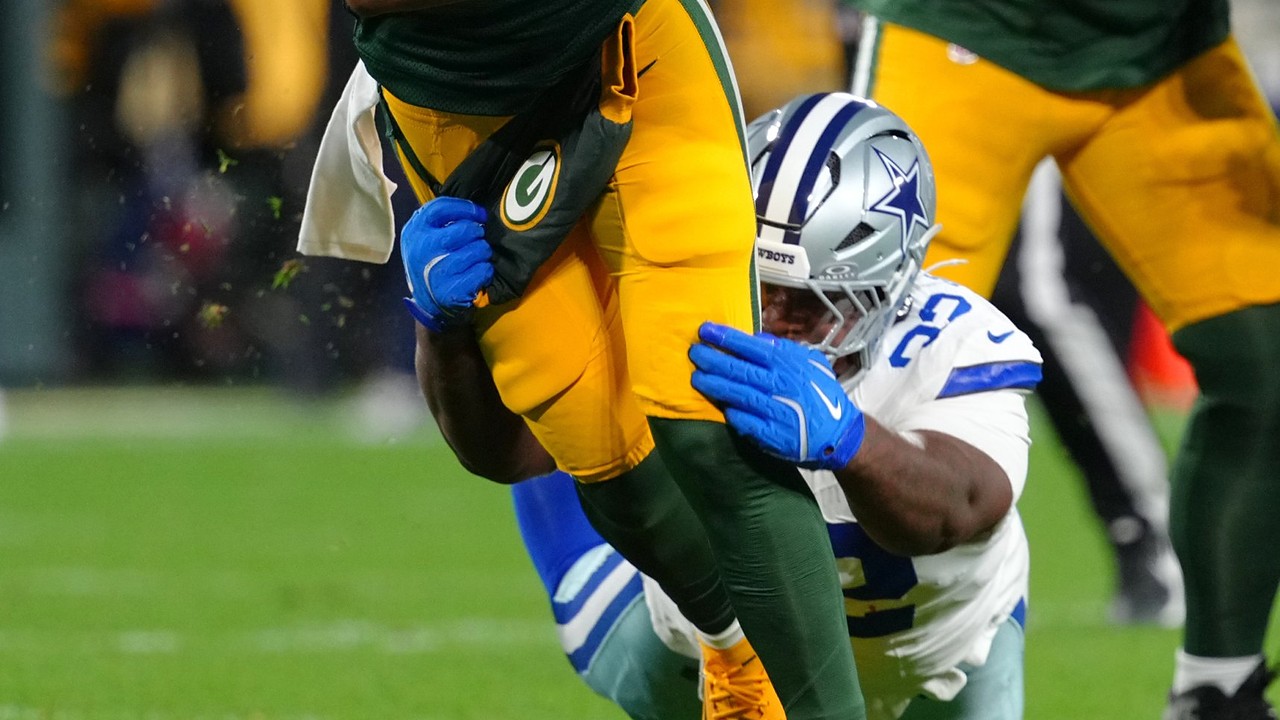 Dallas Cowboys defensive tackle Quinnen Williams grabs the legs of the Green Bay Packers quarterback with both gloved hands.