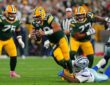 Green Bay Packers quarterback Jordan Love scrambles as Dallas Cowboys defensive tackle Quinnen Williams grabs at his legs.