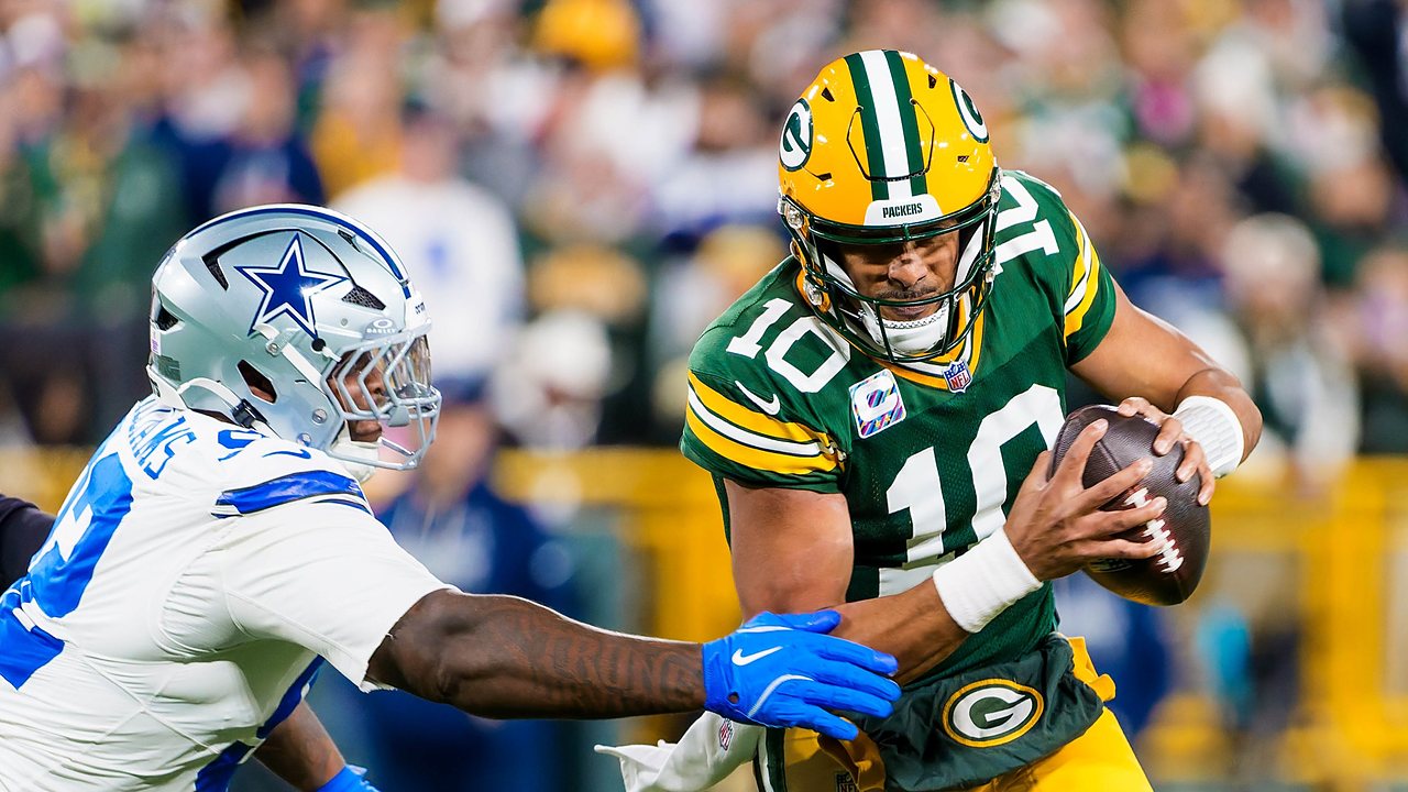 Green Bay Packers quarterback Jordan Love tucks the ball and runs as Dallas Cowboys defensive lineman Quinnen Williams reaches for him.