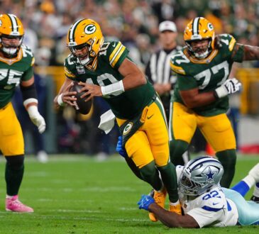 Green Bay Packers quarterback Jordan Love scrambles as Dallas Cowboys defensive tackle Quinnen Williams grabs at his legs.