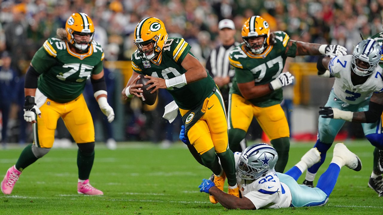 Green Bay Packers quarterback Jordan Love scrambles as Dallas Cowboys defensive tackle Quinnen Williams grabs at his legs.