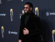 Former NFL quarterback Russell Wilson smiles on the NFL Honors red carpet in sunglasses and a black velvet suit.
