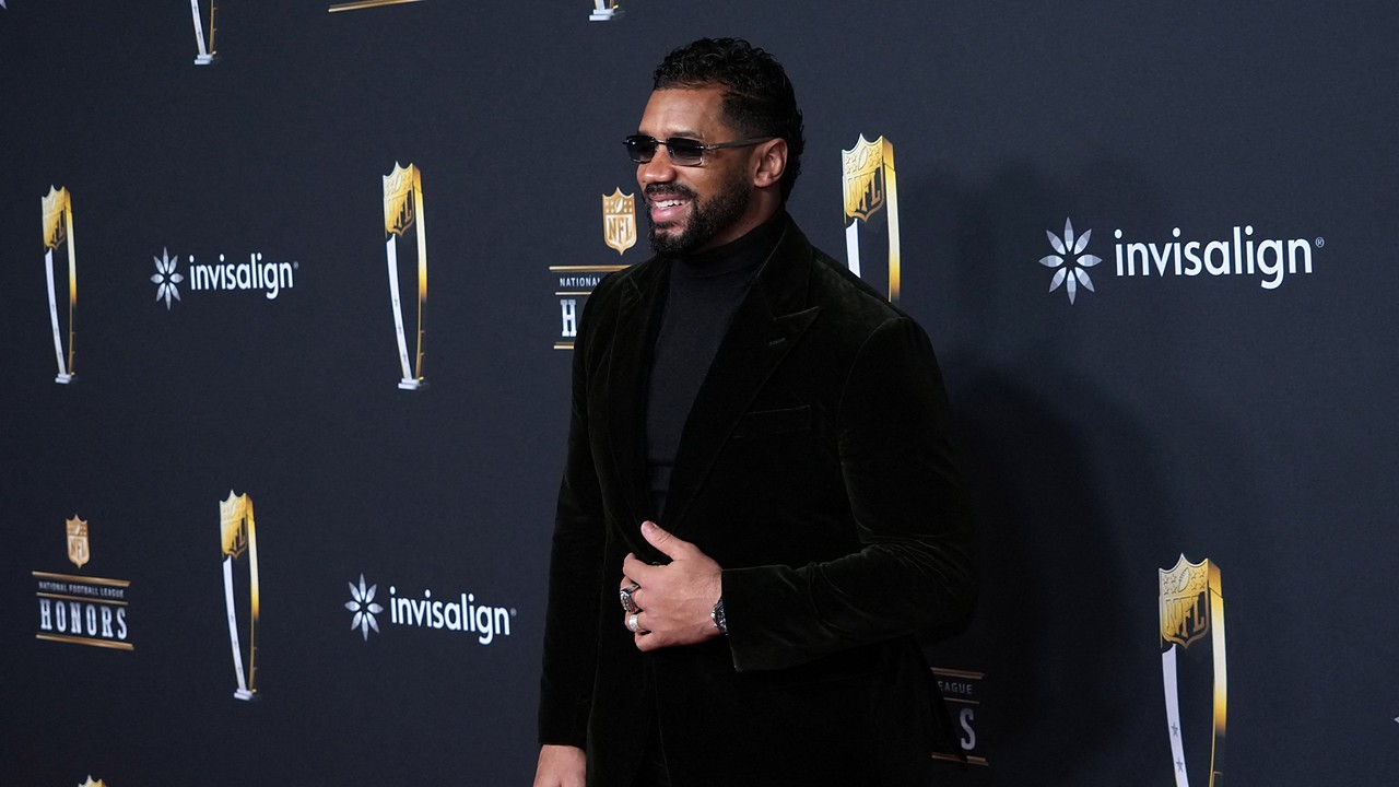 Former NFL quarterback Russell Wilson smiles on the NFL Honors red carpet in sunglasses and a black velvet suit.