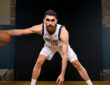 Dallas Mavericks forward-center Santi Aldama crouches in a dribbling stance with a basketball during a media day portrait.