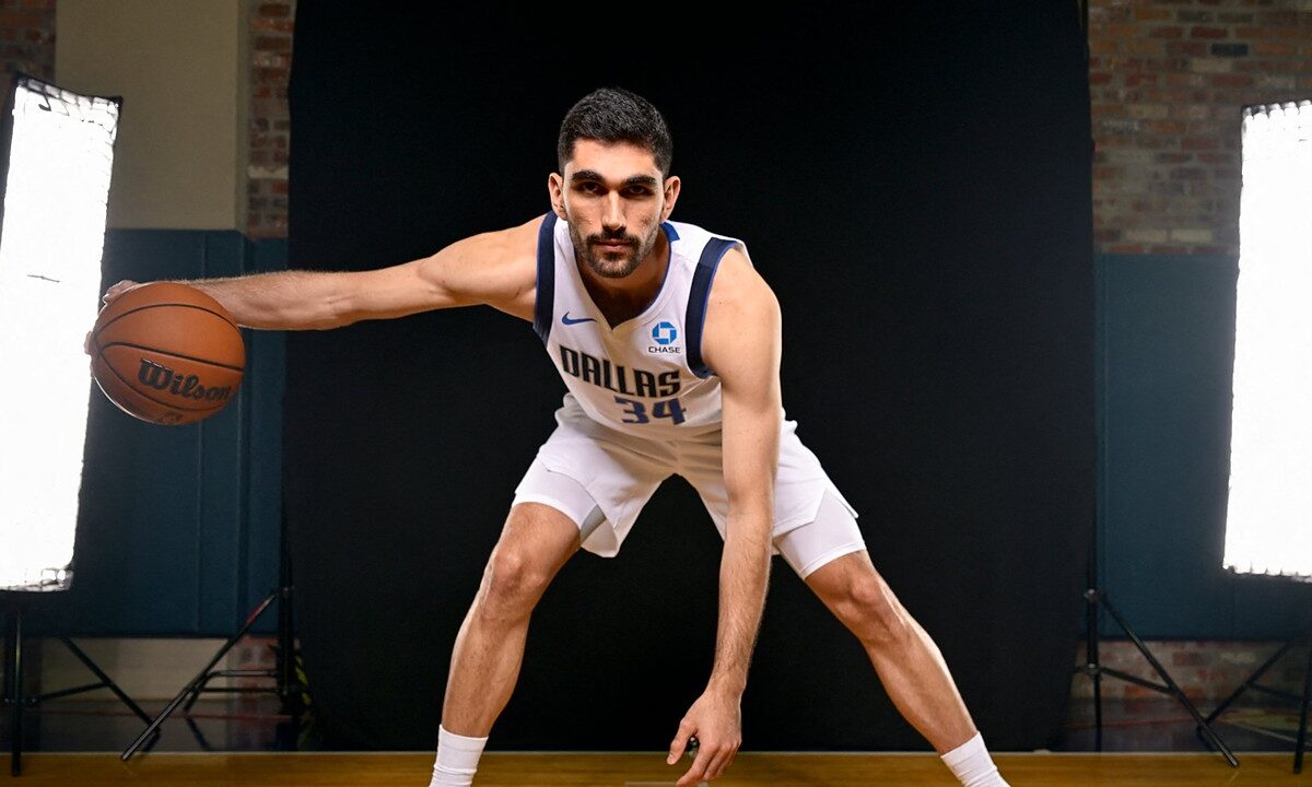 Dallas Mavericks forward-center Santi Aldama crouches in a dribbling stance with a basketball during a media day portrait.