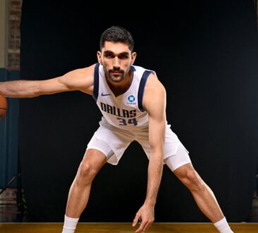 Dallas Mavericks forward-center Santi Aldama crouches in a dribbling stance with a basketball during a media day portrait.
