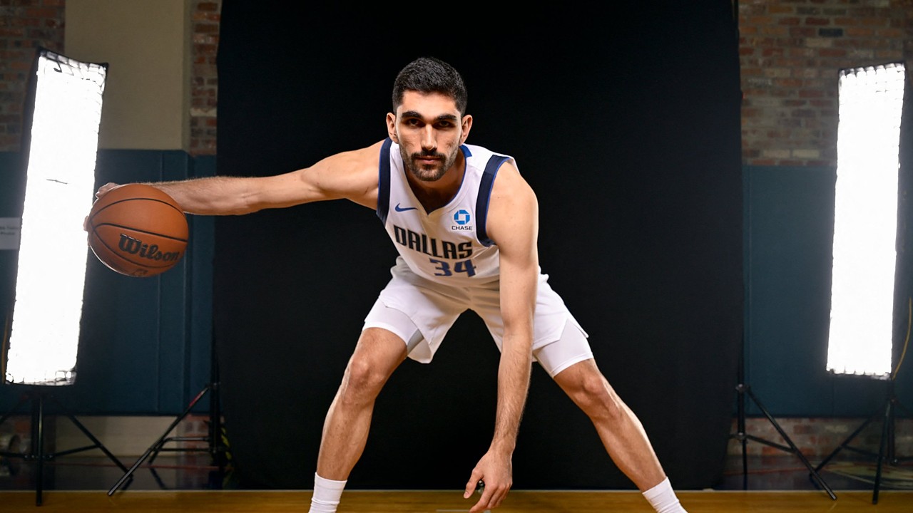 Dallas Mavericks forward-center Santi Aldama crouches in a dribbling stance with a basketball during a media day portrait.