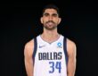 Dallas Mavericks forward-center Santi Aldama smiles with his hands behind his back in a white Dallas No. 34 jersey.
