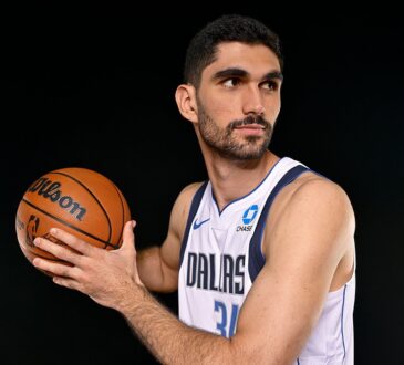 Dallas Mavericks forward-center Santi Aldama holds a basketball in shooting position and looks off to his left.
