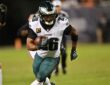 Philadelphia Eagles running back Saquon Barkley carries the ball upfield with a teammate and a defender trailing.