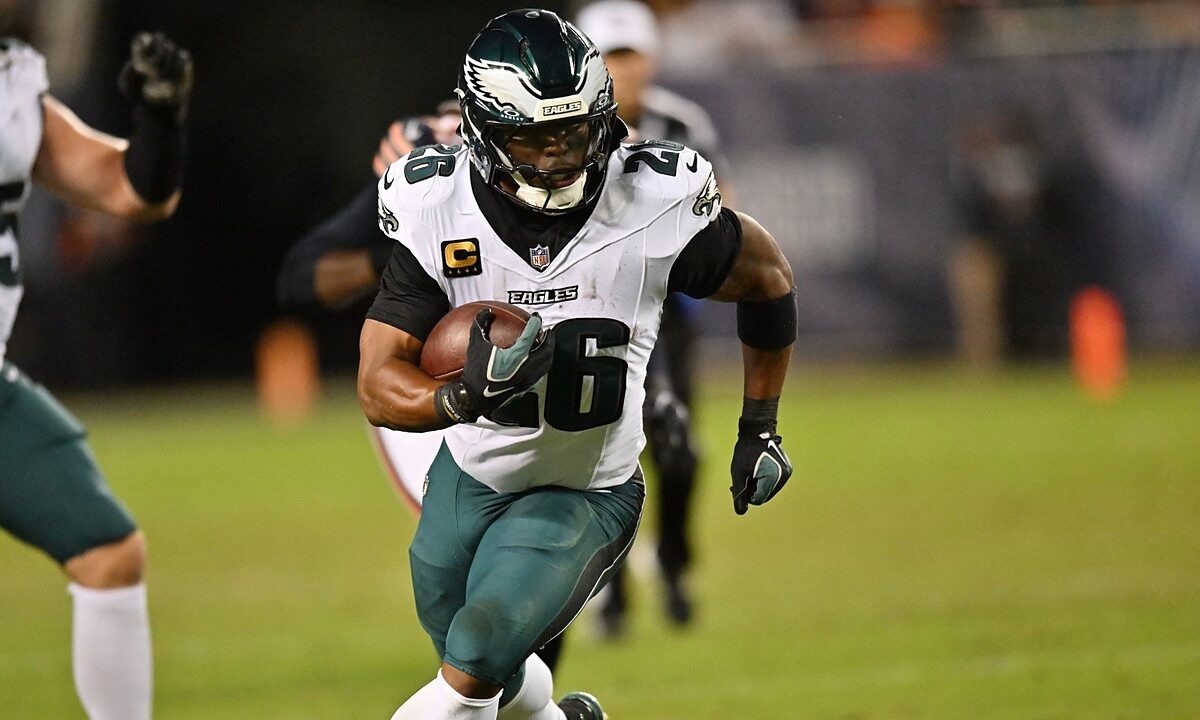 Philadelphia Eagles running back Saquon Barkley carries the ball upfield with a teammate and a defender trailing.