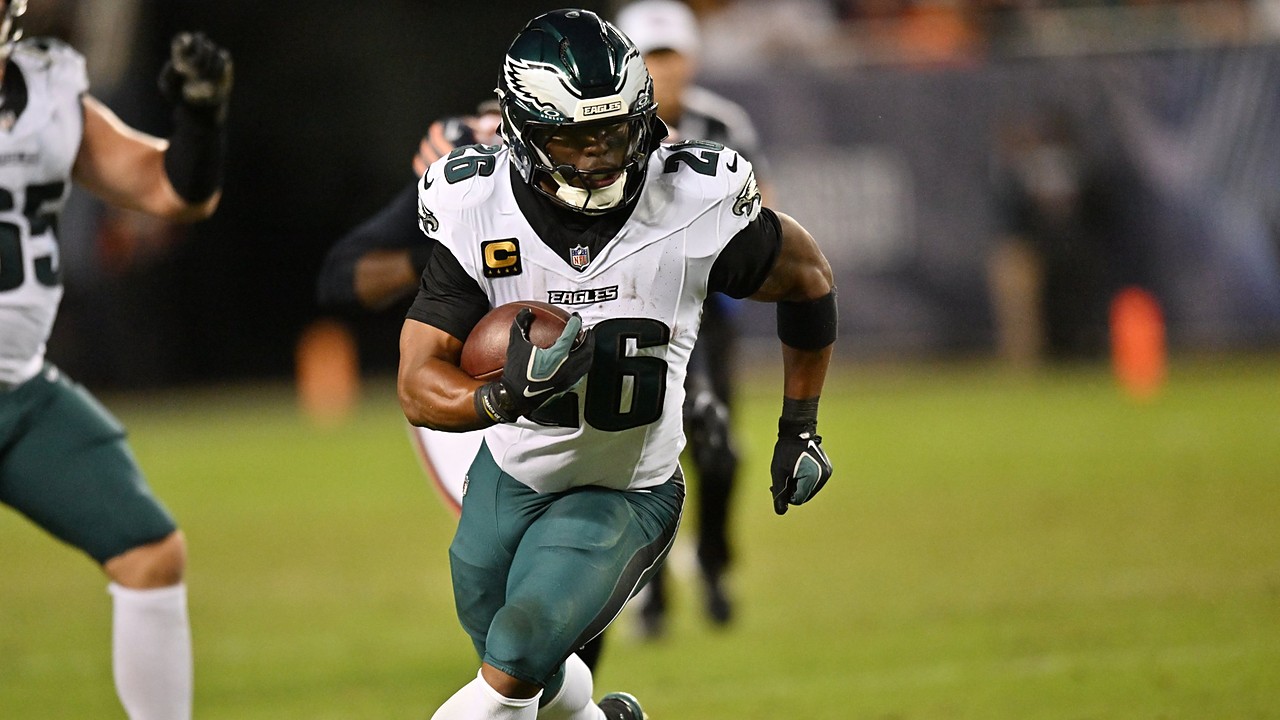 Philadelphia Eagles running back Saquon Barkley carries the ball upfield with a teammate and a defender trailing.