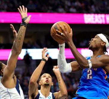 Oklahoma City Thunder guard Shai Gilgeous-Alexander rises for a shot as two Dallas Mavericks defenders reach up to contest.