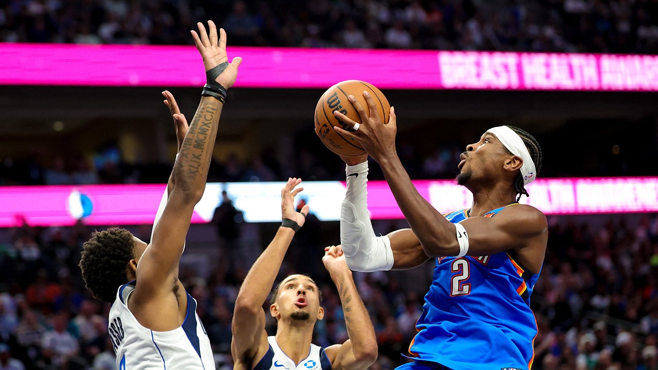 Oklahoma City Thunder guard Shai Gilgeous-Alexander rises for a shot as two Dallas Mavericks defenders reach up to contest.