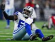 Dallas Cowboys linebacker Shemar James sits on the turf and raises one hand toward the sideline.