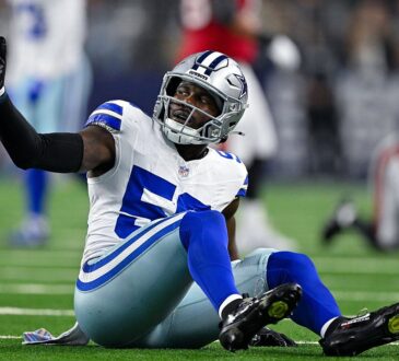 Dallas Cowboys linebacker Shemar James sits on the turf and raises one hand toward the sideline.