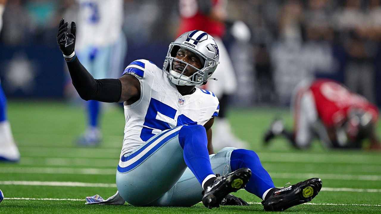 Dallas Cowboys linebacker Shemar James sits on the turf and raises one hand toward the sideline.