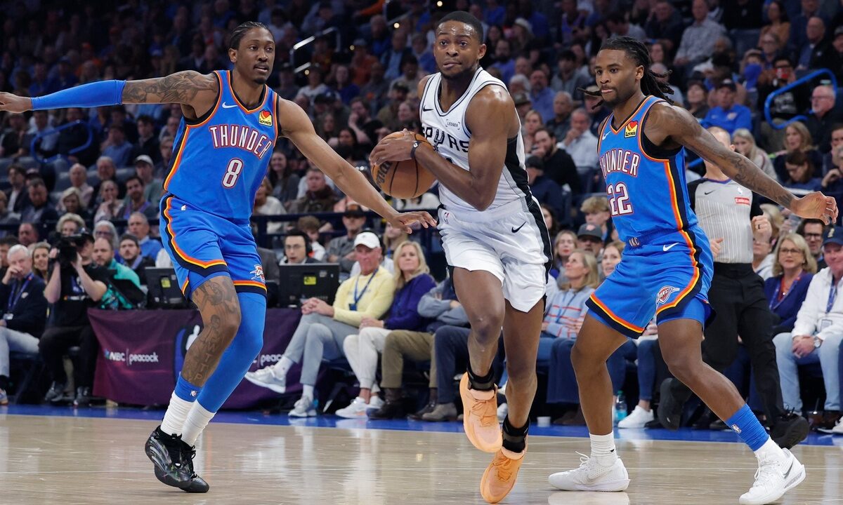 San Antonio Spurs guard De'Aaron Fox #4 drives between Oklahoma City Thunder defenders Jalen Williams #8 and Cason Wallace #22 at Paycom Center.