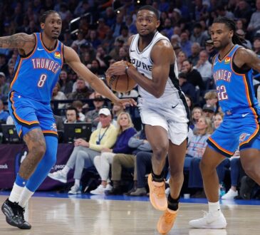 San Antonio Spurs guard De'Aaron Fox #4 drives between Oklahoma City Thunder defenders Jalen Williams #8 and Cason Wallace #22 at Paycom Center.