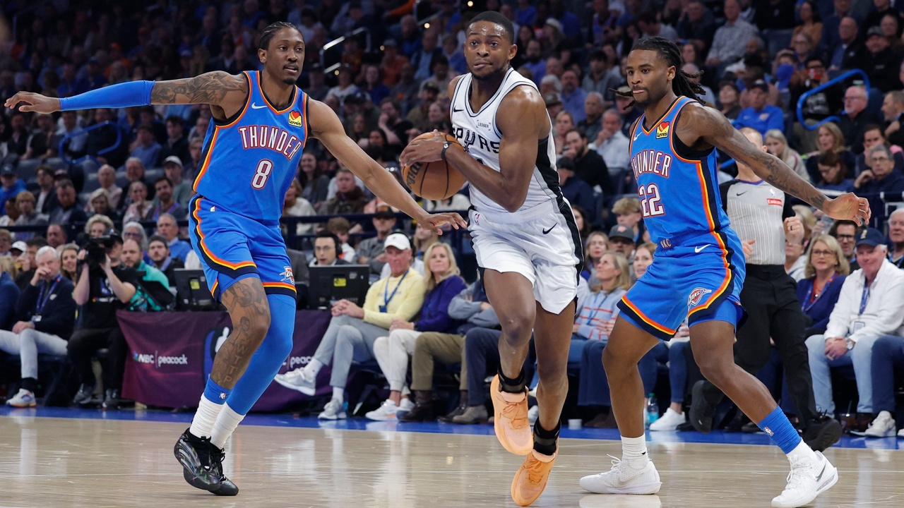 San Antonio Spurs guard De'Aaron Fox #4 drives between Oklahoma City Thunder defenders Jalen Williams #8 and Cason Wallace #22 at Paycom Center.