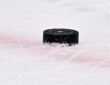 A black NHL game puck bearing the Dallas Stars logo sits on the ice near a red line.