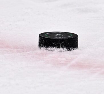 A black NHL game puck bearing the Dallas Stars logo sits on the ice near a red line.