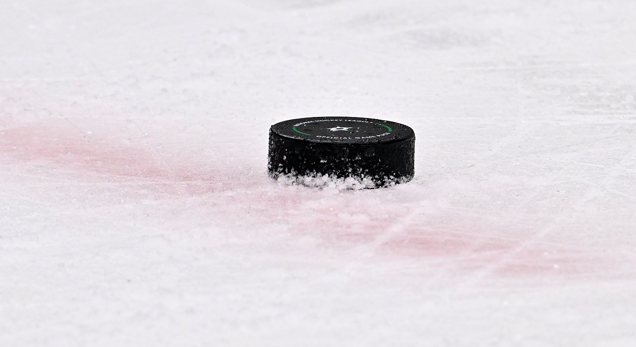 A black NHL game puck bearing the Dallas Stars logo sits on the ice near a red line.