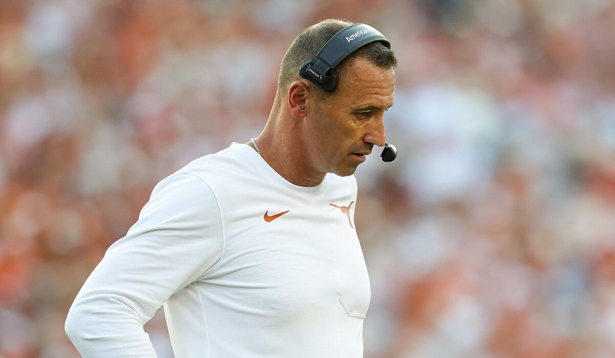 Texas head coach Steve Sarkisian looks down with a hand on his hip while wearing a headset on the sideline.