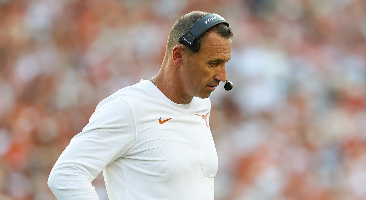 Texas head coach Steve Sarkisian looks down with a hand on his hip while wearing a headset on the sideline.