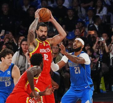Houston Rockets center Steven Adams holds the ball overhead as Dallas Mavericks center Daniel Gafford defends him.