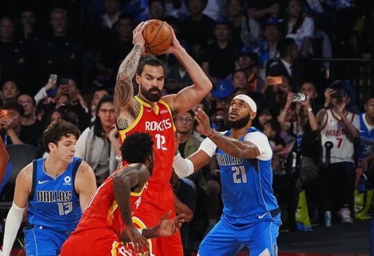 Houston Rockets center Steven Adams holds the ball overhead as Dallas Mavericks center Daniel Gafford defends him.