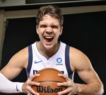 Dallas Mavericks forward Tarik Biberović yells while gripping a basketball with both hands in a white Dallas jersey.