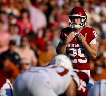 Oklahoma place kicker Tate Sandell adjusts his shoulder pads while lining up a field goal behind the line.