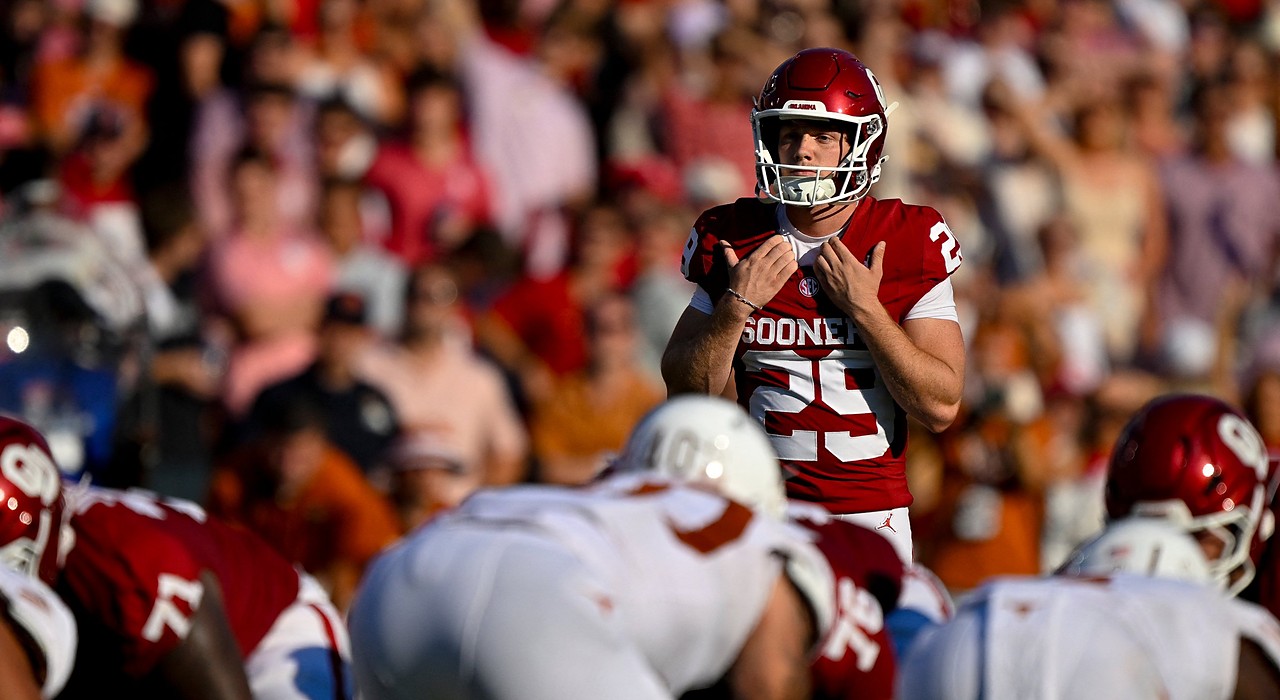 Oklahoma place kicker Tate Sandell adjusts his shoulder pads while lining up a field goal behind the line.
