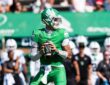 North Texas quarterback Tayven Jackson drops back with the ball in both hands, scanning the field in an all-green uniform.