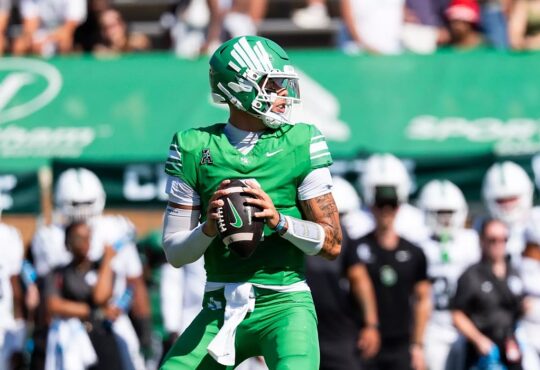 North Texas quarterback Tayven Jackson drops back with the ball in both hands, scanning the field in an all-green uniform.