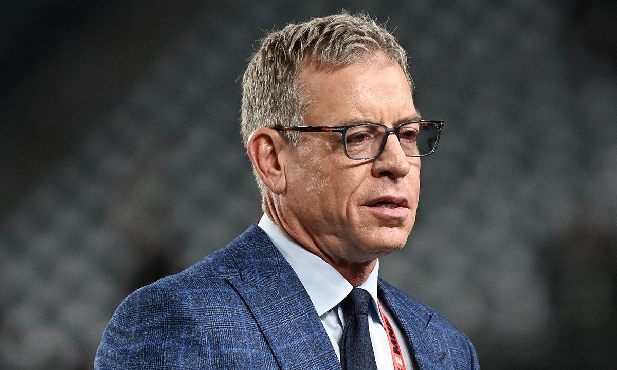 Former Dallas Cowboys quarterback Troy Aikman, in glasses and a blue plaid suit, looks on before the game.