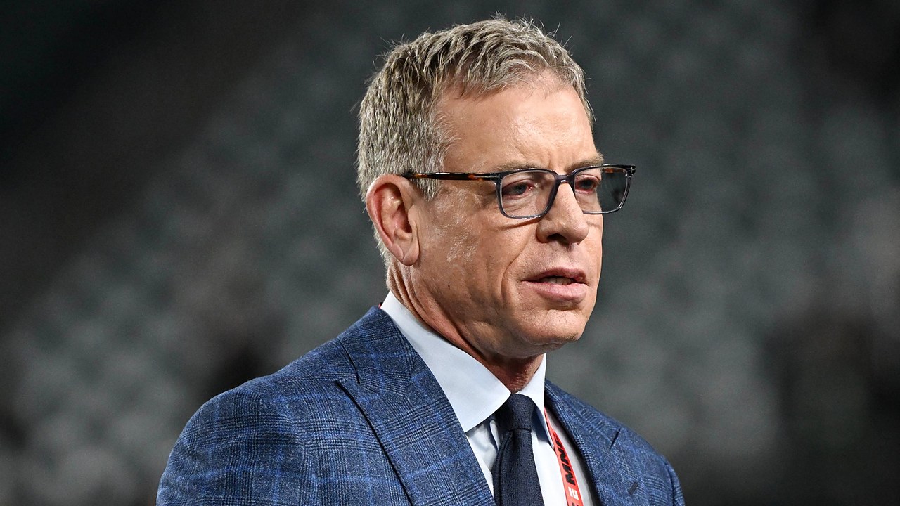 Former Dallas Cowboys quarterback Troy Aikman, in glasses and a blue plaid suit, looks on before the game.